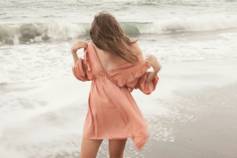 a woman standing on top of a beach next to the ocean, inspired by Anna Boch, pexels contest winner, renaissance, flowing salmon-colored silk, back pose, puff sleeves, desaturated