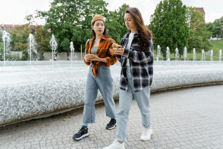 two women standing next to each other near a fountain, trending on pexels, baggy jeans, having a snack, wearing correct era clothes, flannel