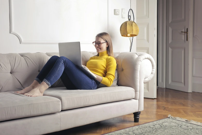 a woman sitting on a couch using a laptop, inspired by Constantin Hansen, trending on pexels, figuration libre, yellow carpeted, french provincial furniture, reading glasses, angled shot