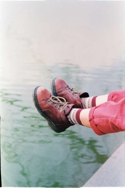 a close up of a person's feet near a body of water, a polaroid photo, maroon doc marten boots, color film, maroon red, wearing kneesocks