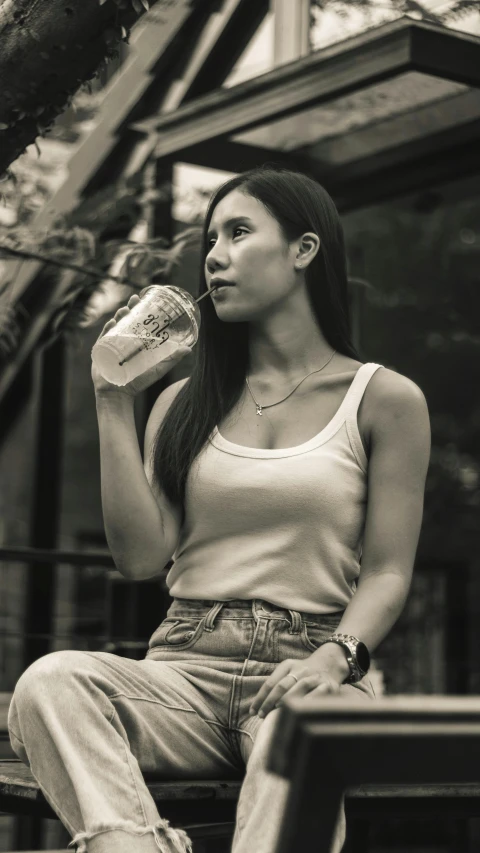 a woman sitting on a bench drinking from a bottle, a black and white photo, inspired by Tan Ting-pho, trending on pexels, photorealism, iced latte, sleeveless, wearing casual clothes, sittin