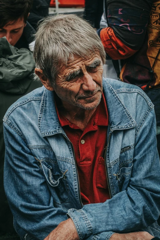 a man sitting in front of a crowd of people, pexels contest winner, photorealism, jean jacket, wrinkles, grumpy [ old ], a high angle shot