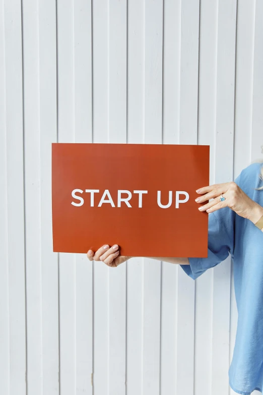 a woman holding a sign that says start up, an album cover, stock photograph, healthcare, thumbnail, brown