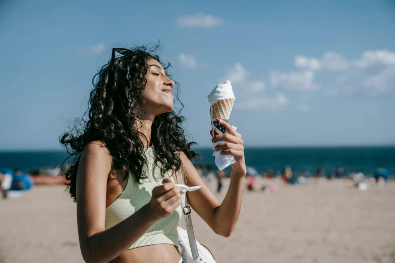 a woman eating an ice cream cone on the beach, a photo, trending on pexels, happening, indian girl with brown skin, wavy hair spread out, skincare, 🍸🍋