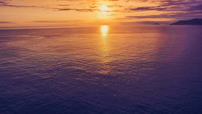 a large body of water with a sunset in the background, pexels contest winner, ariel view, calm ocean, screensaver, violet and yellow sunset