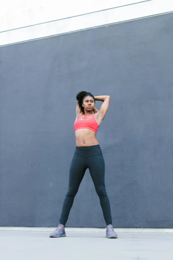 a woman standing in front of a gray wall, by Jessie Algie, pexels contest winner, arabesque, wearing fitness gear, alanis guillen, wearing crop top, head tilted down