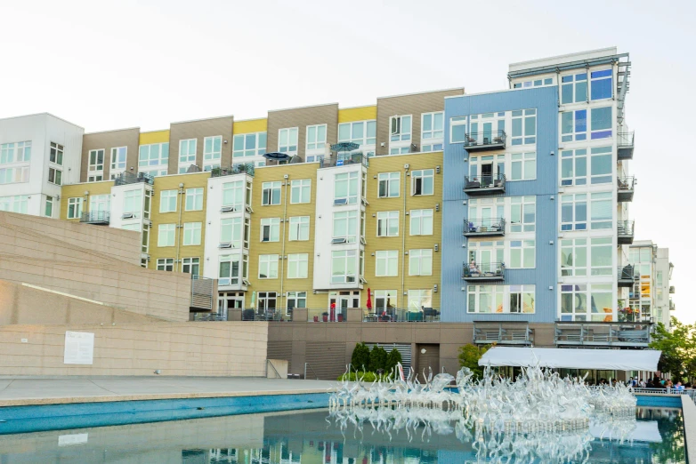 a building with a fountain in front of it, inspired by Washington Allston, unsplash, modernism, ten flats, poolside, viewed from the harbor, multicolored