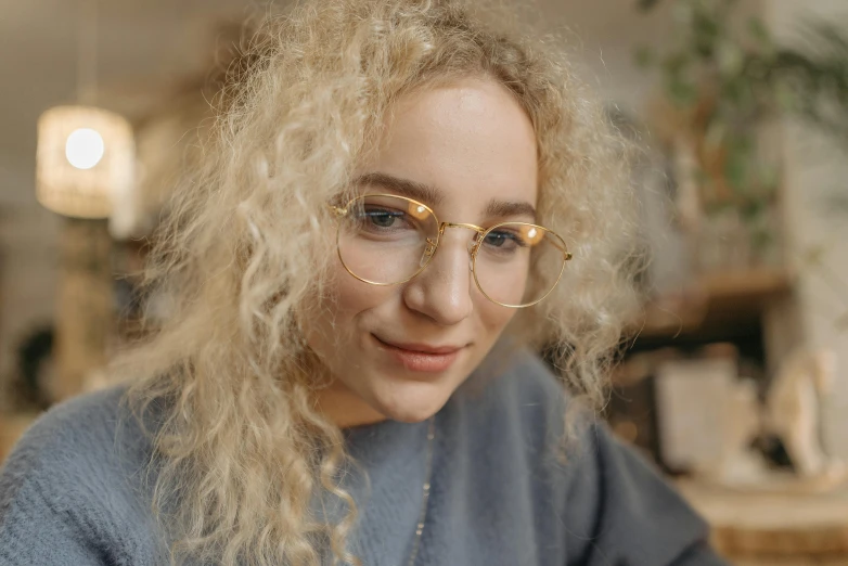 a woman sitting at a table using a cell phone, a character portrait, trending on pexels, photorealism, blonde curly hair, gold glasses, selfie photo, rounded eyeglasses