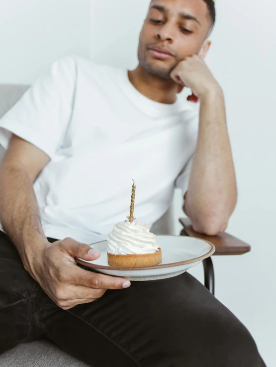 a man sitting in a chair holding a plate with a cake on it, inspired by Barthélemy Menn, trending on unsplash, non binary model, holding a candle, profile image, lean man with light tan skin