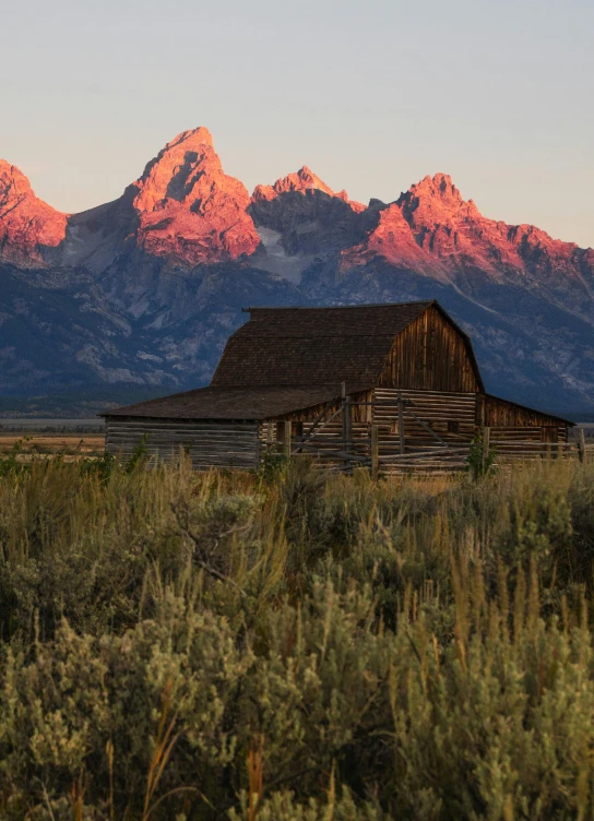 a barn in a field with mountains in the background, a portrait, by Randall Schmit, unsplash contest winner, photographer art wolfe, evening sunlight, tall stone spires, crimson