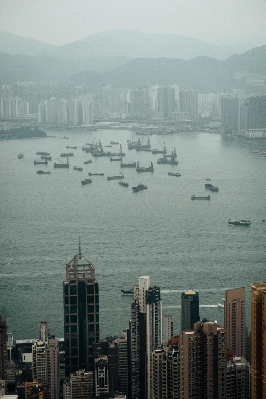 a large body of water surrounded by tall buildings, a tilt shift photo, happening, ships with sails, haze, hong kong, no crop