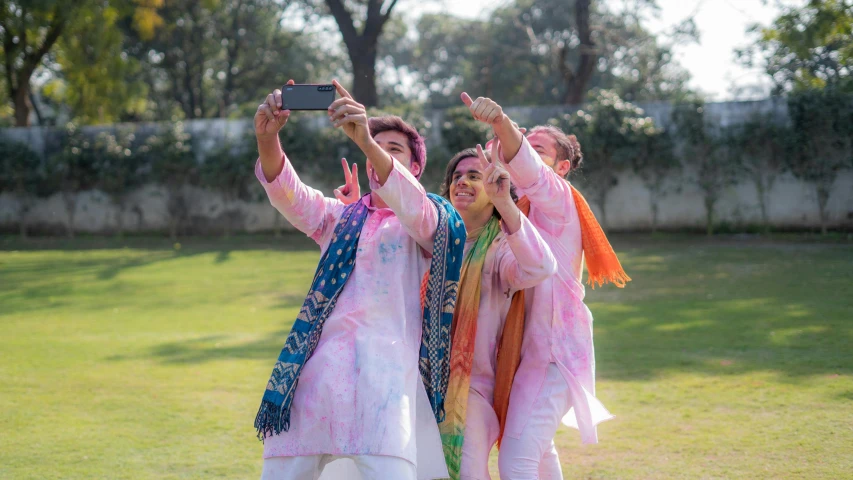 a group of people standing on top of a lush green field, a picture, wearing festive clothing, hold up smartphone, pink and blue colour, wearing a silk kurta