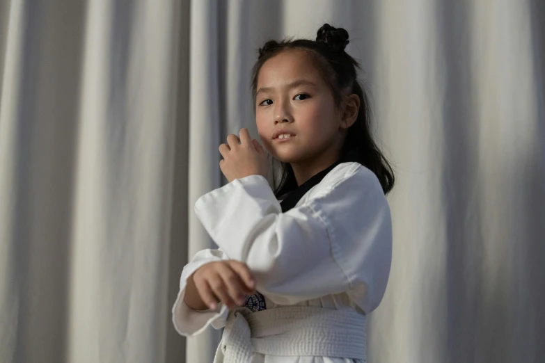 a little girl standing in front of a curtain, inspired by Chen Lu, pexels contest winner, martial art pose, robe. perfect faces, manuka, young asian woman