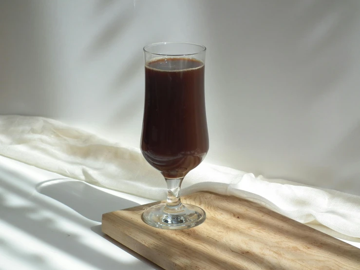 a glass of coffee sitting on top of a wooden board, inspired by Nyuju Stumpy Brown, unsplash, photorealism, juice, jakarta, bright daylight indoor photo, fully chocolate