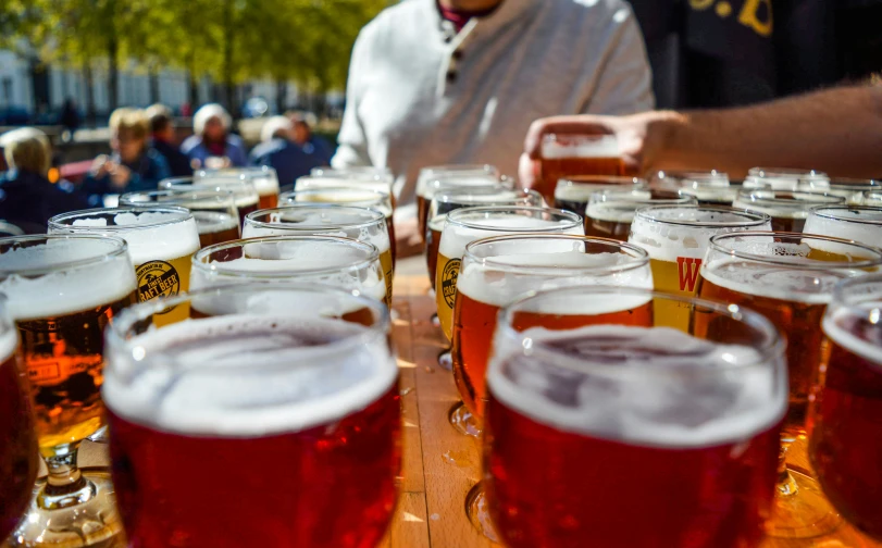 a row of beer glasses sitting on top of a wooden table, by Washington Allston, pexels contest winner, al fresco, holding court, red brown and white color scheme, group of seven