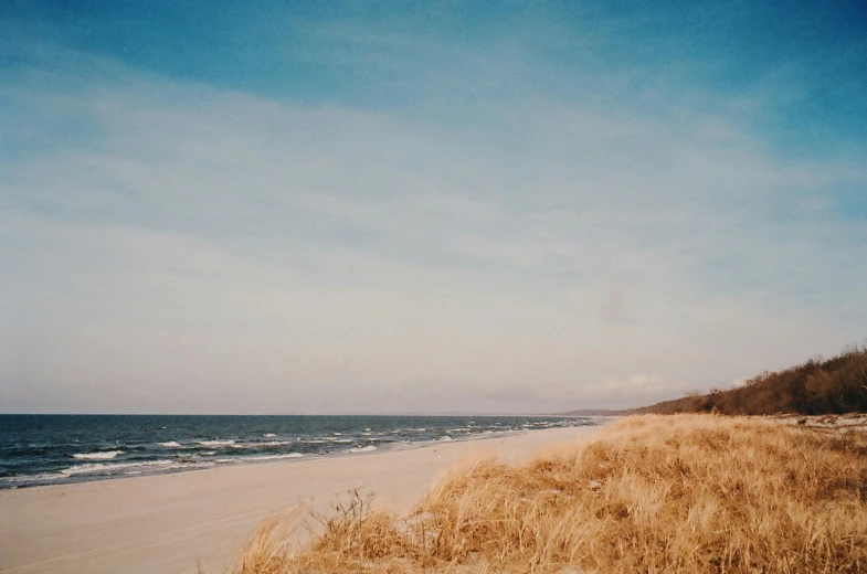 a man standing on top of a sandy beach next to the ocean, a polaroid photo, by Anna Boch, unsplash, minimalism, autumn season, hasselblad photograph, sparsely populated, on a canva