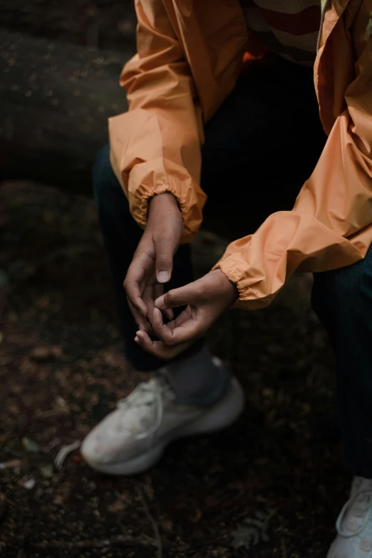 a woman sitting on a log in the woods, inspired by Elsa Bleda, trending on unsplash, orange jacket, hands of men, overcast, hand gesture