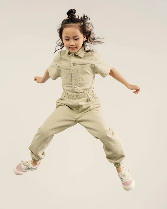 a little girl that is jumping in the air, an album cover, inspired by Weiwei, unsplash, cargo pants, beige, jumpsuit, pokimane