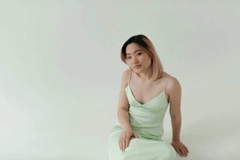 a woman sitting on the floor in a green dress, inspired by Russell Dongjun Lu, trending on pexels, on a pale background, half asian, looking straight, andy park