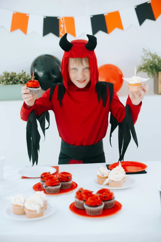 a little girl in a devil costume sitting at a table with cupcakes, pexels, teenage boy, cooked, gif, very