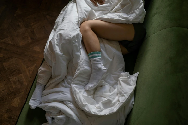 a woman laying on top of a green couch covered in a blanket, inspired by Elsa Bleda, pexels contest winner, antipodeans, wearing kneesocks, white sheets, ignant, small bed not made