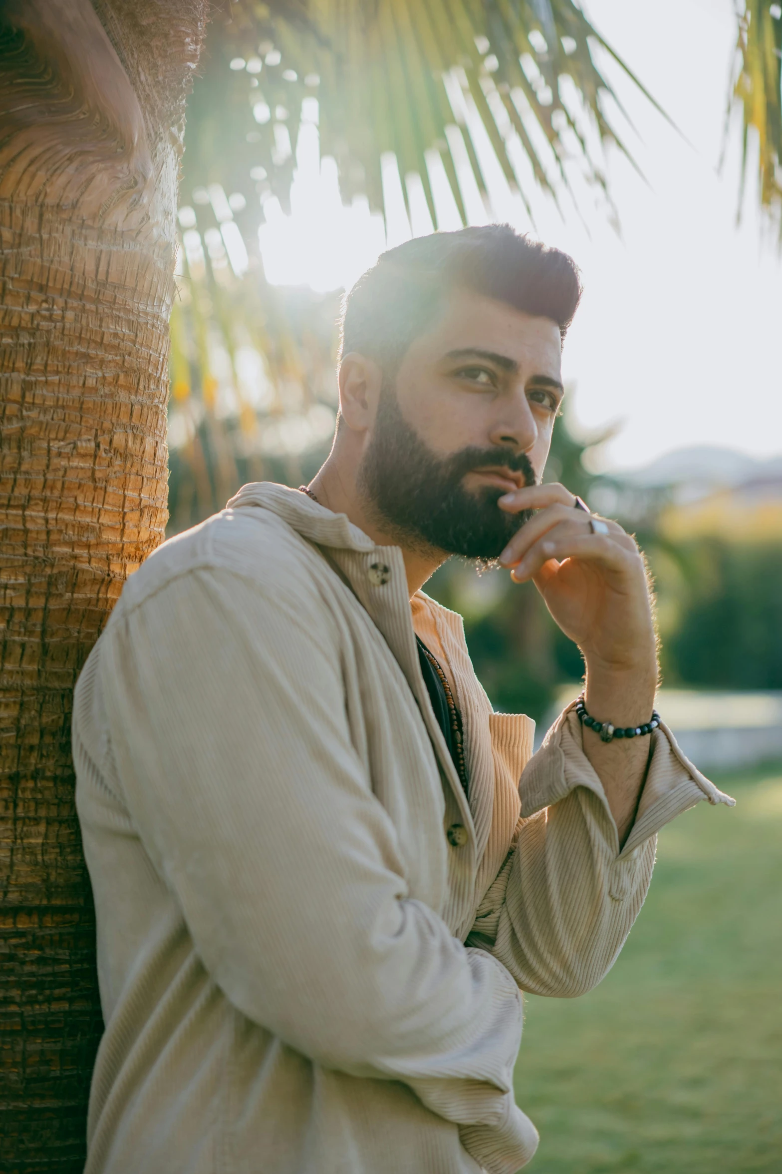 a man standing next to a palm tree talking on a cell phone, an album cover, by Ismail Acar, pexels contest winner, bearded beautiful man, thoughtful pose, sitting, sunfaded