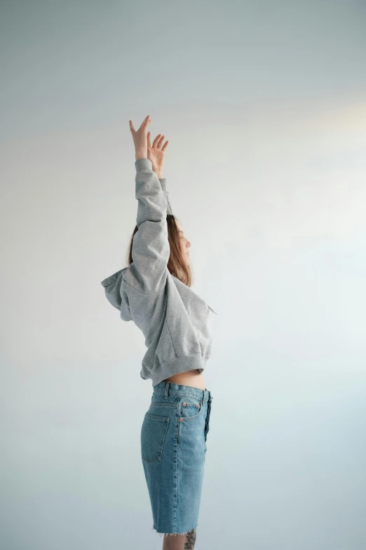 a woman reaching up to catch a frisbee, trending on unsplash, minimalism, wearing a grey hooded sweatshirt, wearing a cropped top, looking upwards, denim