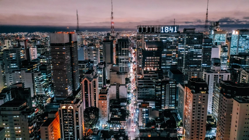 an aerial view of a city at night, by Luis Miranda, pexels contest winner, avenida paulista, youtube thumbnail, early evening, towering over a city
