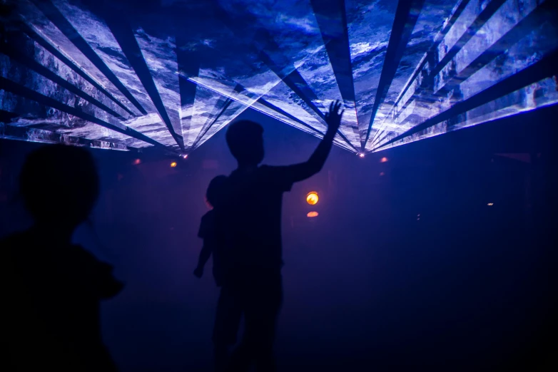 a couple of people that are standing in the dark, interactive art, looking at the ceiling, rave, silhouette of a man, walking down