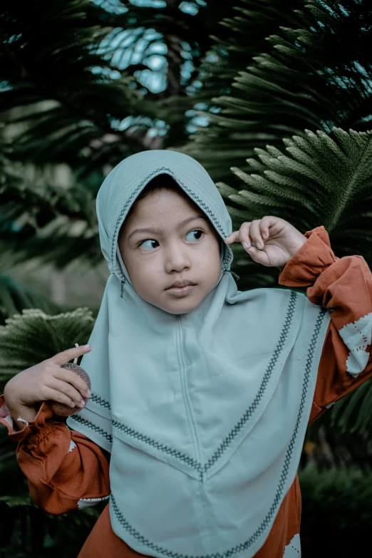 a close up of a child wearing a hijab, a colorized photo, by Basuki Abdullah, unsplash contest winner, grey orange, muted green, shrugging, square