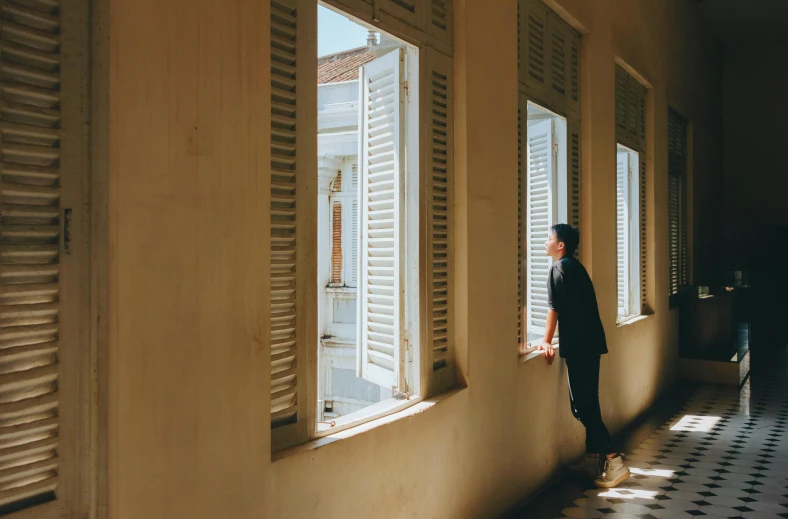 a woman looking out of a window in a building, inspired by Steve McCurry, pexels contest winner, colonial style, man standing, set on singaporean aesthetic, shutters