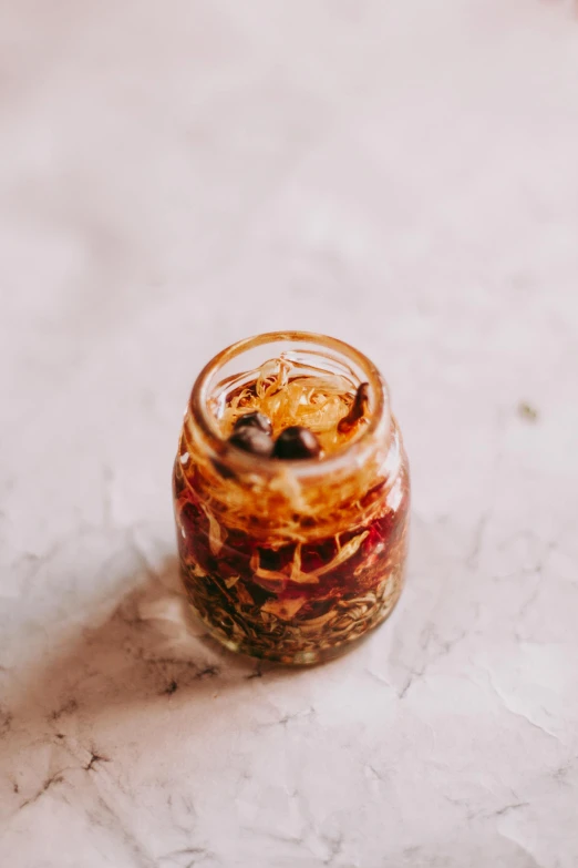 a close up of a jar of food on a table, by Jessie Algie, dried petals, smoked layered, olive oil, drink