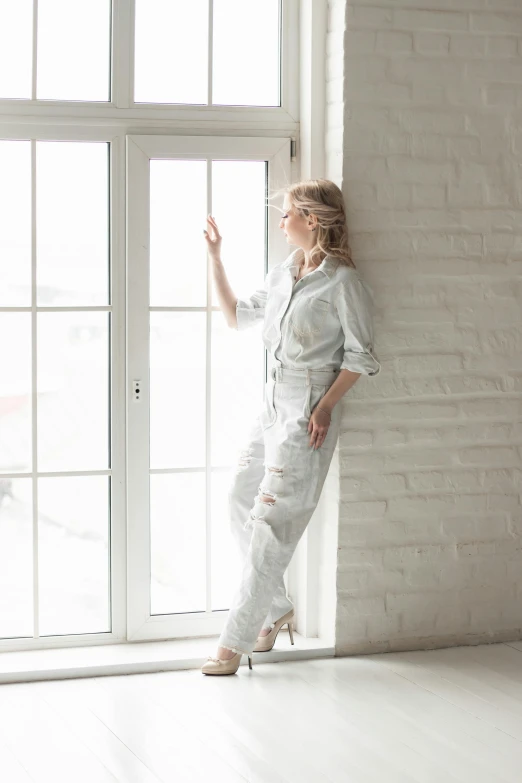 a woman standing next to a window in a room, inspired by Dóra Keresztes, light and space, wearing human air force jumpsuit, distressed, white and silver, trending on imagestation