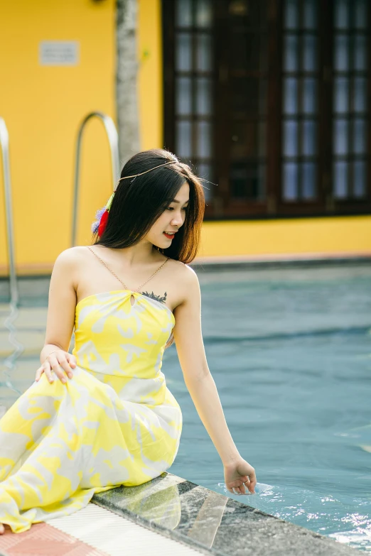 a woman sitting on the edge of a swimming pool, a portrait, inspired by Xie Sun, unsplash, lady using yellow dress, vietnamese woman, tube-top dress, portrait mode photo