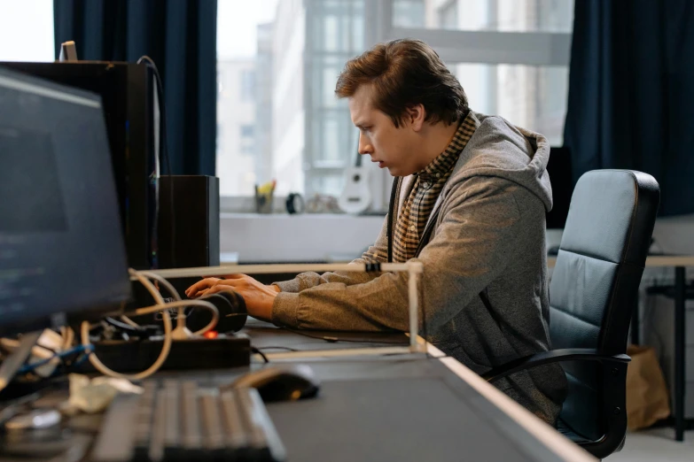 a man sitting at a desk working on a computer, by Adam Marczyński, pexels, video - game, casually dressed, looking serious, thicc