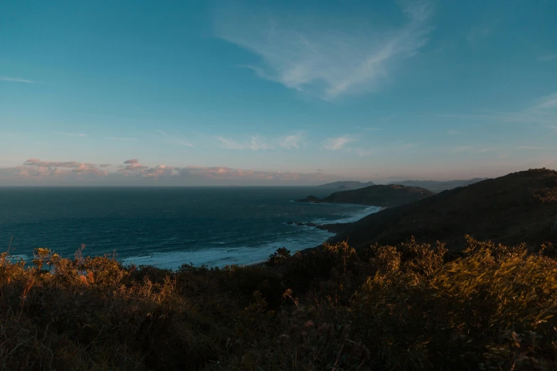 a view of the ocean from the top of a hill, by Thomas Furlong, unsplash contest winner, twilight ; wide shot, hills and ocean, late afternoon, low - angle shot