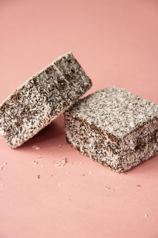 two pieces of chocolate sitting on top of a pink surface, super fluffy, grey, heavy grain, coconuts