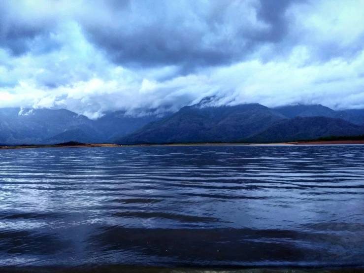 a large body of water with mountains in the background, by Charlotte Harding, hurufiyya, ominous photo, wet climate, snapchat photo, under blue clouds