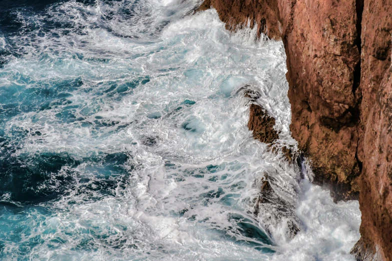 a man standing on top of a cliff next to the ocean, pexels contest winner, process art, rushing water, brown, aquamarine, abstract photography