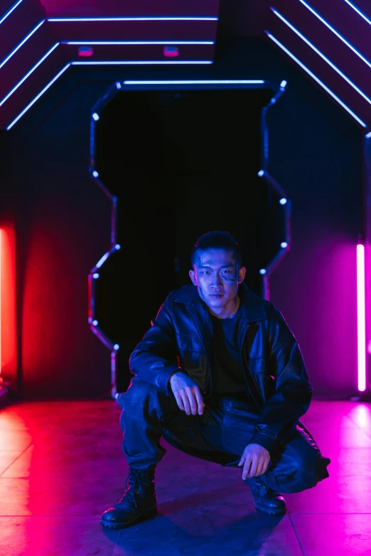 a man sitting on the ground in front of neon lights, inspired by Feng Zhu, standing with a black background, official store photo, symetrical scene, sythwave