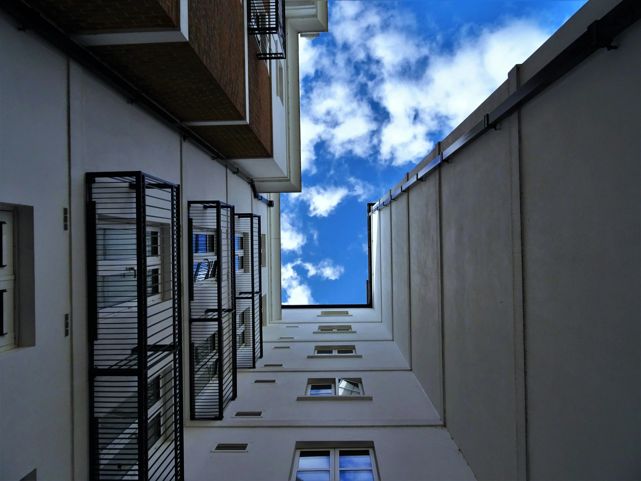 a tall white building with a blue sky in the background, a photo, inspired by Leandro Erlich, unsplash, modernism, alleys, view from ground, ( few clouds ), outside intricate