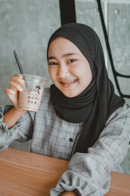 a woman sitting at a table with a drink in her hand, inspired by JoWOnder, hurufiyya, drink milkshakes together, wearing casual clothing, q hayashida, young teen