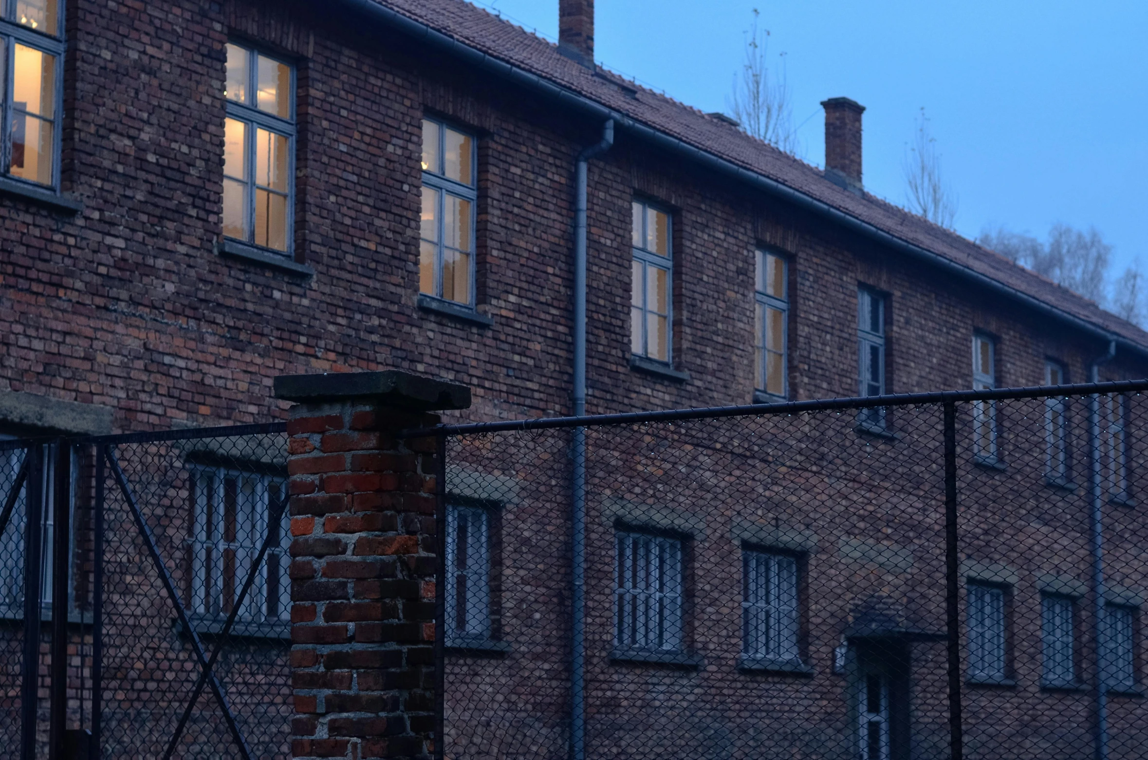 a red fire hydrant sitting in front of a brick building, by Adam Marczyński, pexels contest winner, auschwitz camp, large windows to forest at night, 1940s photo, gallows