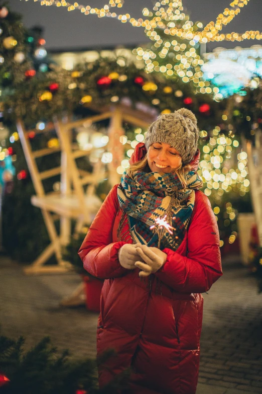 a woman standing in front of a christmas tree, warm lantern lighting, sparklers, wearing a red gilet, grey