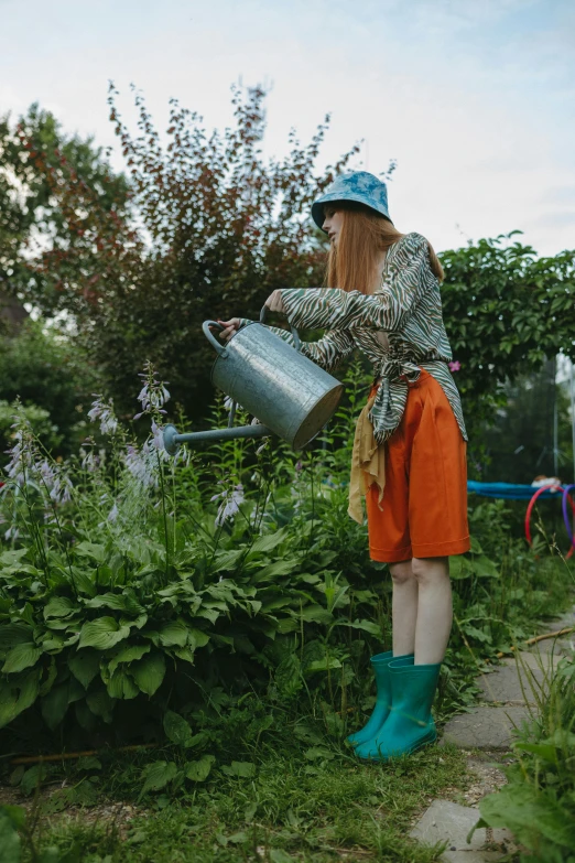 a woman that is standing in the grass with a watering can, inspired by Elsa Beskow, pexels contest winner, teal and orange colours, garden at home, wearing overalls, super long shot