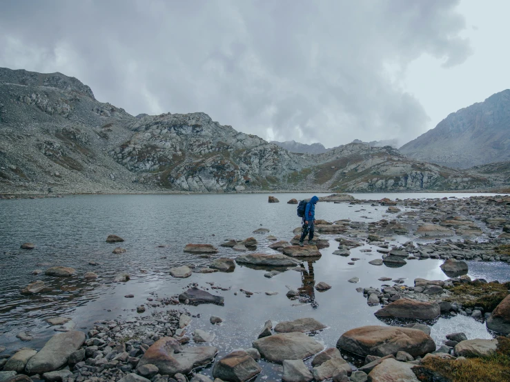 a person standing on rocks near a body of water, alpine climate, maintenance photo, overcast lake, graeme base