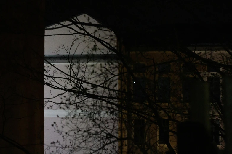 a view of a building through a window at night, by Attila Meszlenyi, some trees in the corner, view from ground, white building, barely visible from the shadows
