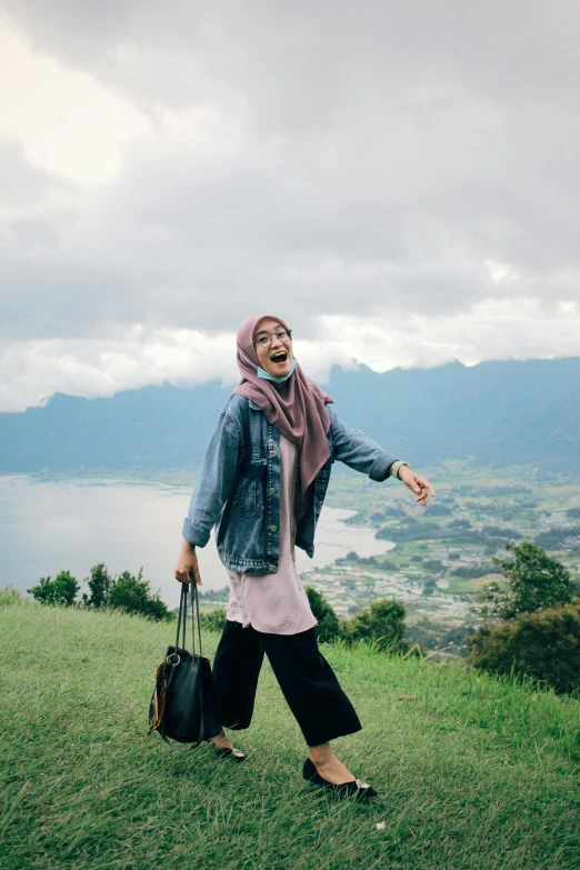 a woman standing on top of a lush green hillside, by Basuki Abdullah, trending on unsplash, mutahar laughing, hijab, near a lake, walking