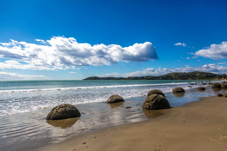 a beach filled with lots of rocks next to the ocean, globes, new zealand landscape, round clouds, in a row