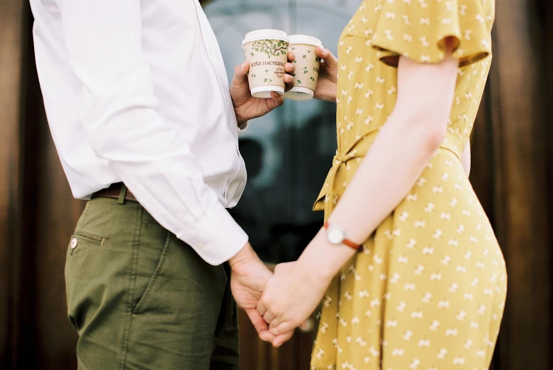 a man standing next to a woman holding a cup of coffee, by Julia Pishtar, trending on pexels, yellow and olive color scheme, holding hands, sydney hanson, romantic lead